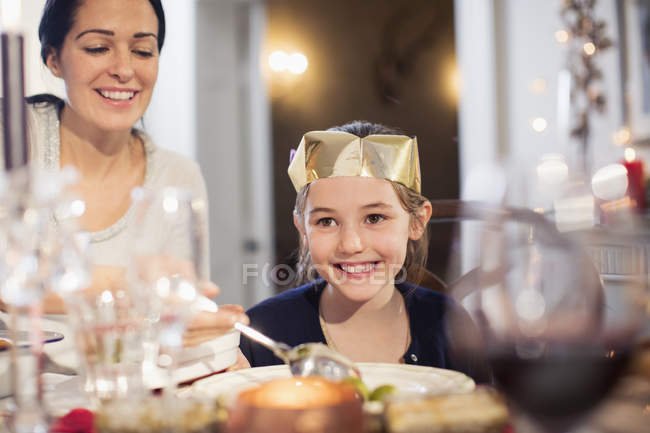 Усміхнена мати і дочка в паперовій короні насолоджуються різдвяною вечерею — стокове фото