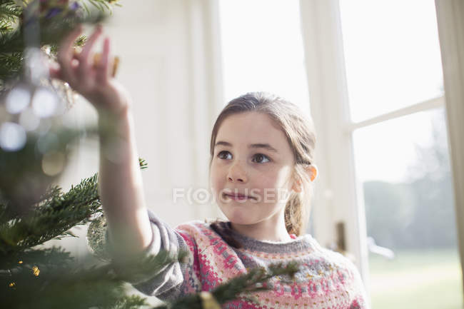 Chica curiosa tocando ornamento en el árbol de Navidad - foto de stock