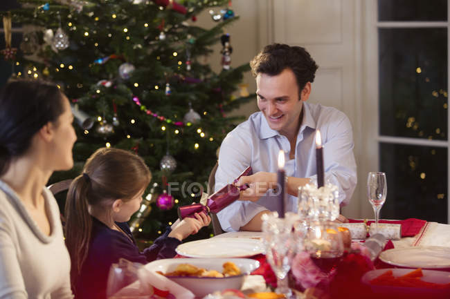 Отец и дочь тянут рождественский крекер за столом при свечах — стоковое фото