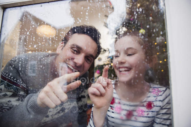Father and daughter drawing in condensation on wet winter window — Stock Photo