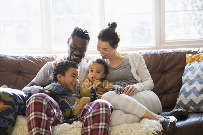 Multi-ethnic young family relaxing in pajamas on living room sofa — Stock Photo