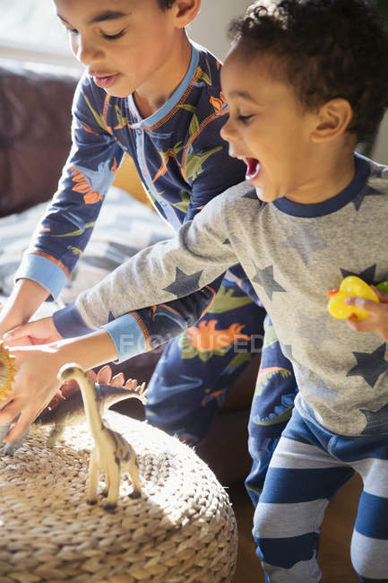 Irmãos de pijama brincando com brinquedos de dinossauro — Fotografia de Stock