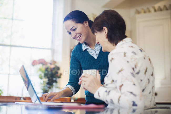 Hija y madre mayor utilizando el ordenador portátil en la cocina - foto de stock