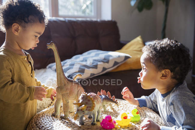 Niños hermanos jugando con dinosaurios y juguetes de pato de goma - foto de stock