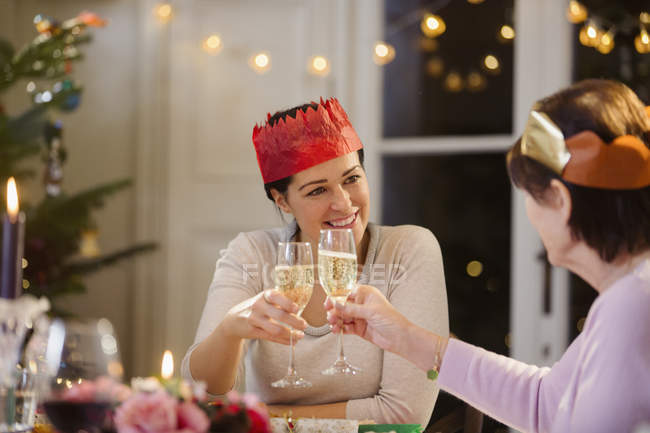 Filha e mãe sênior em coroas de papel brindando taças de champanhe na mesa de jantar de Natal — Fotografia de Stock