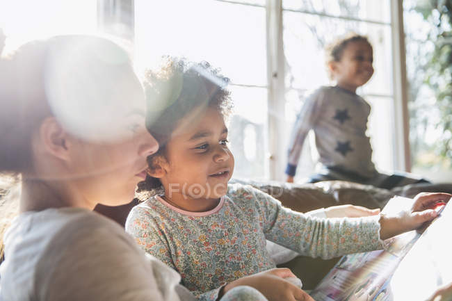 Mother and daughter reading book in sunny living room — Stock Photo