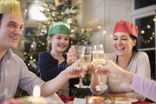 Щаслива родина в паперових ворон тости з водою та келихами шампанського на різдвяній вечері — стокове фото