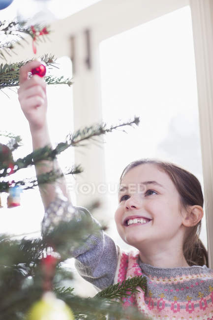 Lächelndes, neugieriges Mädchen berührt Ornament am Weihnachtsbaum — Stockfoto