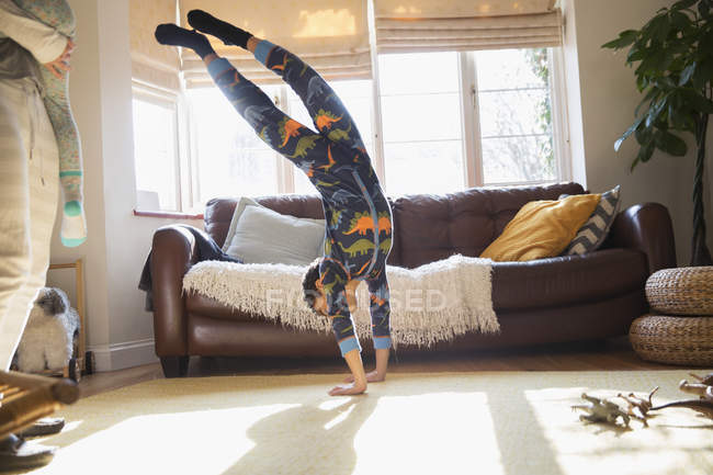 Playful boy in pajamas doing handstand in living room — Stock Photo