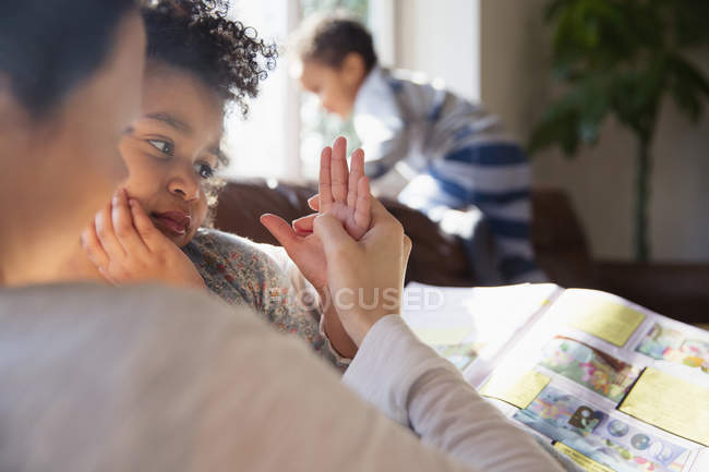 Affectionate mother and daughter holding hands, reading book — Stock Photo