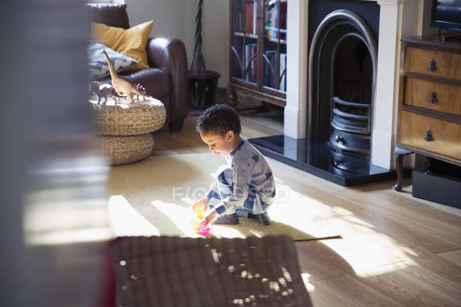 Хлопчик у піжамі грає з іграшками на підлозі вітальні — стокове фото