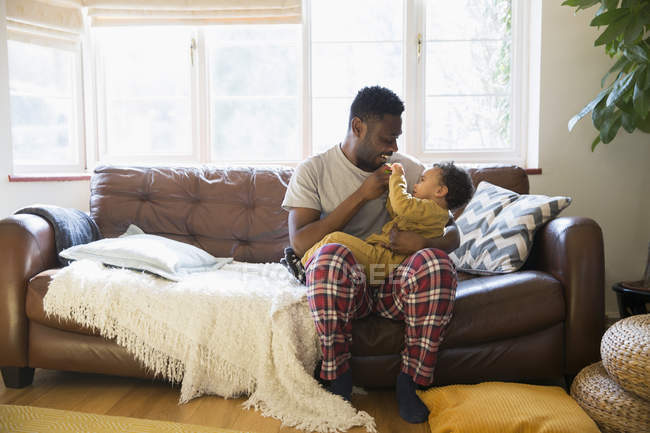 Affectionate father in pajamas cuddling with baby son on living room sofa — Stock Photo