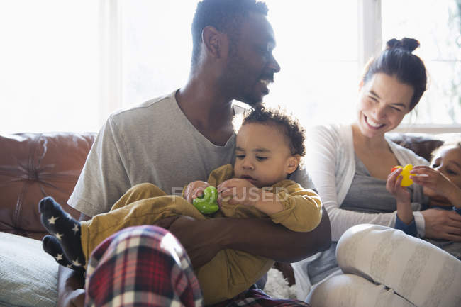 Feliz familia multiétnica en pijama abrazándose en el sofá - foto de stock