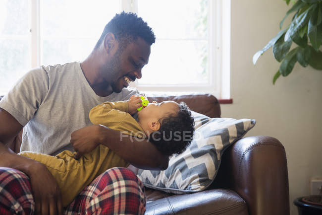 Affectionate father cuddling with baby son on living room sofa — Stock Photo