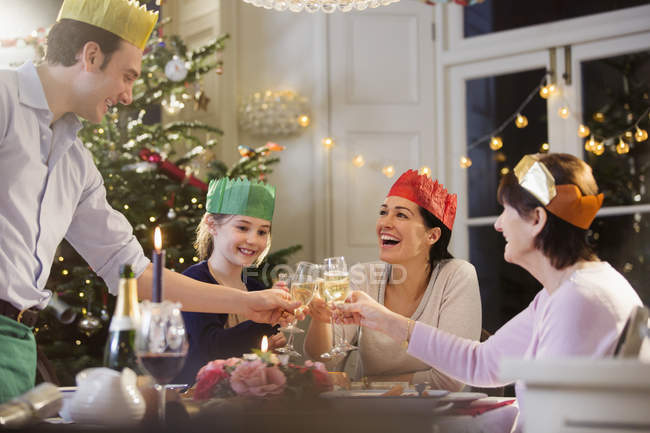 Multi-generation family in paper crowns toasting champagne flutes at candlelight Christmas dinner — Stock Photo