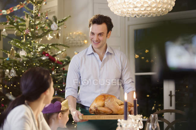 Hombre sirviendo pavo de Navidad a la familia en la mesa de cena a la luz de las velas - foto de stock