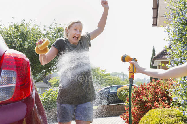 Figlia spruzzatura madre lavaggio auto con tubo — Foto stock