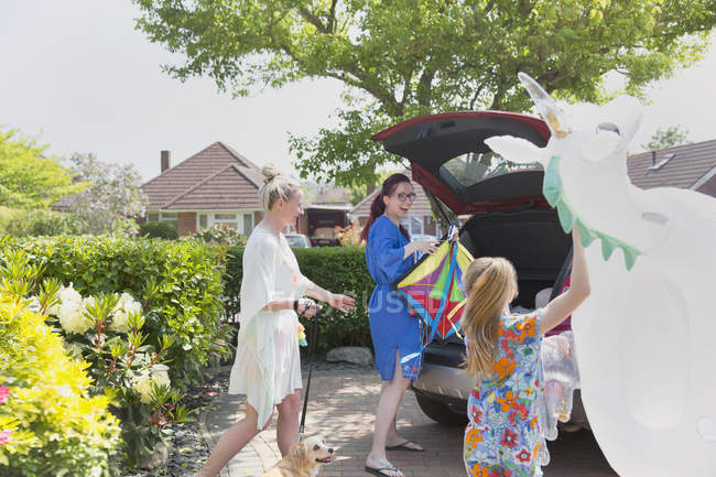 Lesbian couple and daughter loading inflatable unicorn in hatchback of car in driveway — Stock Photo