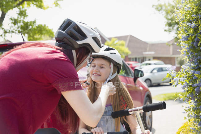 Mother fastening helmet on daughter riding scooter in sunny driveway — Stock Photo