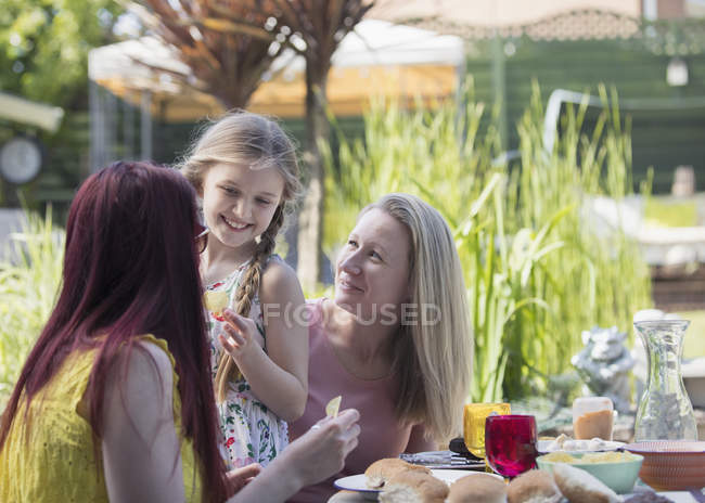 Cariñosa pareja de lesbianas y su hija disfrutando del almuerzo en el patio - foto de stock