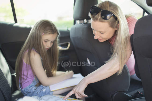 Mère aidant fille faire des devoirs sur le siège arrière de la voiture — Photo de stock