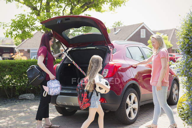 Lesbian couple and daughter loading car for school in sunny driveway — Stock Photo