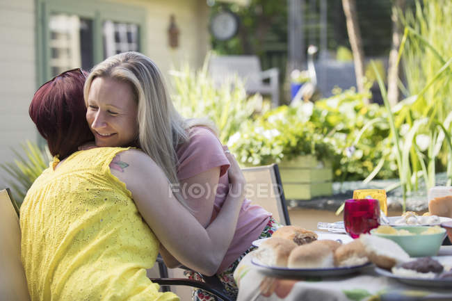 Affectionate lesbian couple hugging at lunch patio table — Stock Photo