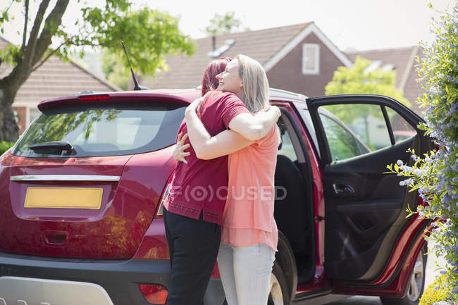Affectionate lesbian couple hugging by car in sunny driveway — Stock Photo