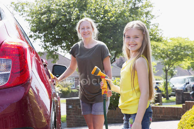 Портрет улыбающейся матери и дочери, моющих машину на солнечной дорожке — стоковое фото