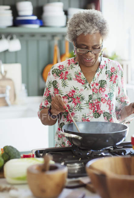 Active senior woman cooking at stove in kitchen — Stock Photo