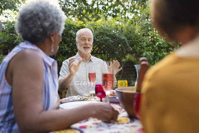 Amis aînés profitant du déjeuner, parlant à la table de patio — Photo de stock