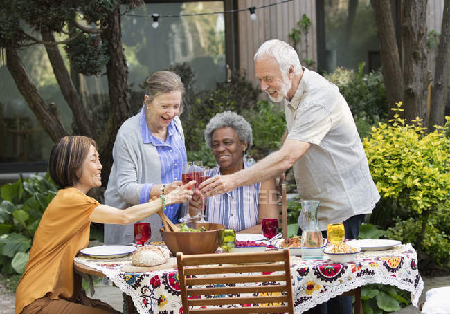 Активные старшие друзья наслаждаются розовым вином и обедом за столом в патио — стоковое фото