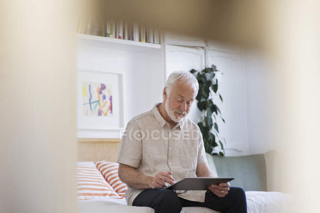 Старший мужчина с помощью цифрового планшета на кровати — стоковое фото