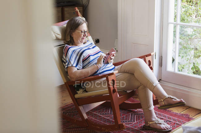 Donna anziana sms con smart phone in sedia a dondolo — Foto stock