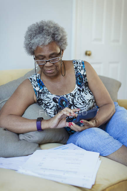 Mujer mayor con calculadora revisando facturas - foto de stock