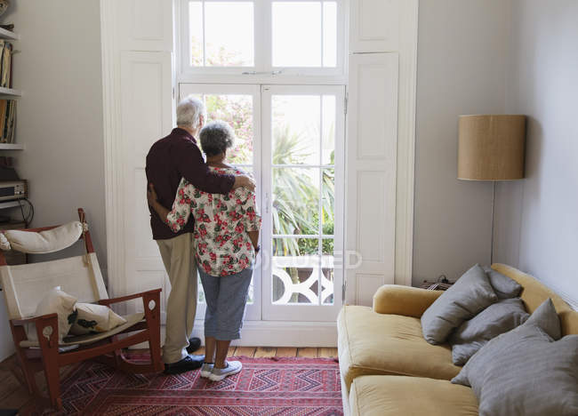 Affettuosa, serena coppia anziana guardando fuori dalla finestra del soggiorno — Foto stock