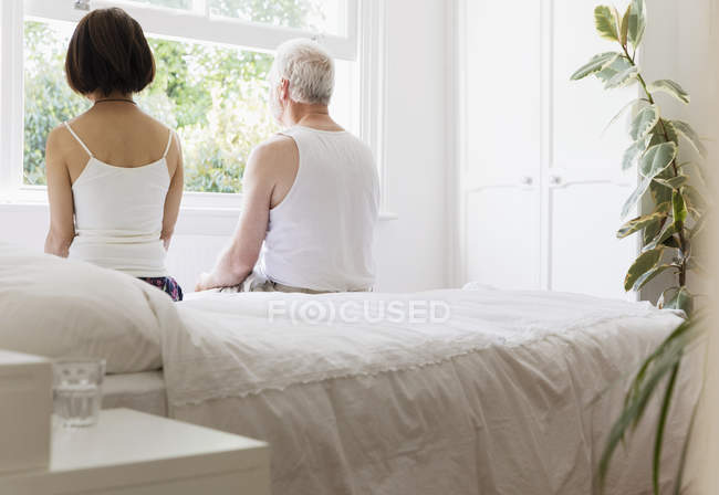 Thoughtful senior couple sitting on bed looking out window — Stock Photo