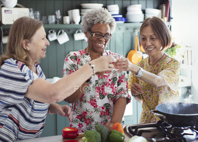 Active senior women friends cooking, toasting cocktails in kitchen — Stock Photo