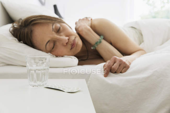 Seniorin schläft im Bett mit Wasser und Medikamenten auf Nachttisch — Stockfoto