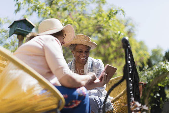 Amis femmes âgées utilisant téléphone intelligent sur terrasse ensoleillée — Photo de stock