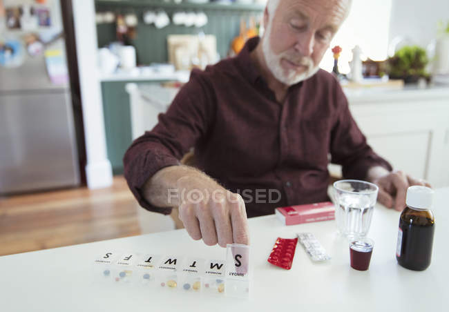 Homem sênior organizando caixa de pílula na mesa da cozinha — Fotografia de Stock