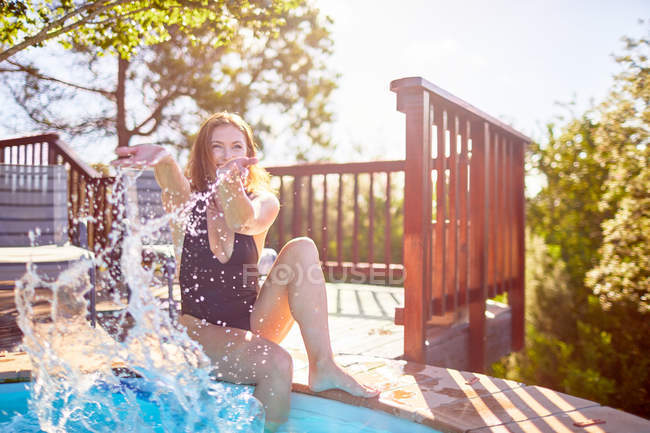 Giovane donna giocosa spruzzi d'acqua a piscina soleggiata — Foto stock