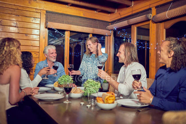 Amici che festeggiano, bevono vino rosso e cenano in cabina — Foto stock