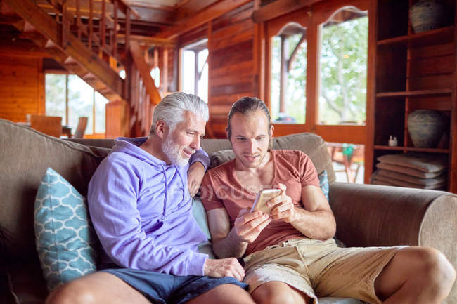 Padre e hijo usando un teléfono inteligente en el sofá de la cabina - foto de stock