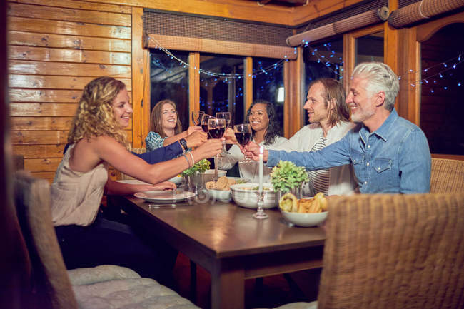 Freunde stoßen mit Rotweingläsern an, genießen das Abendessen am Kabinentisch — Stockfoto