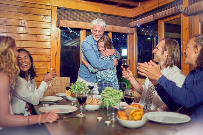 Amis applaudissements pour couple affectueux câlins à la table du dîner — Photo de stock