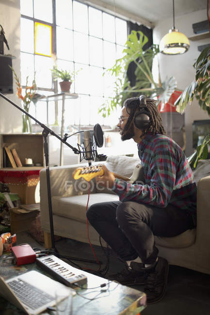 Молодий музикант співає і грає на гітарі, записуючи музику в квартирі — стокове фото