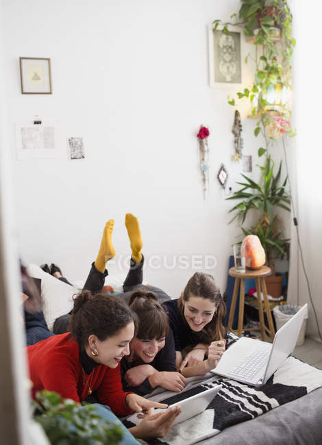Jóvenes estudiantes universitarias que estudian, usando tableta digital y portátil en la cama - foto de stock
