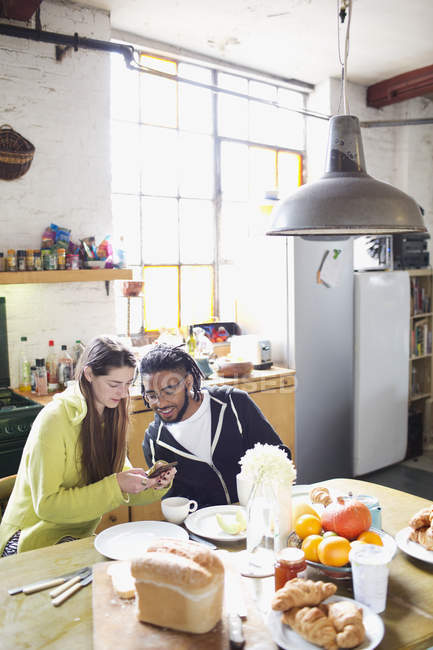 Young couple with smart phone enjoying breakfast in apartment kitchen — Stock Photo