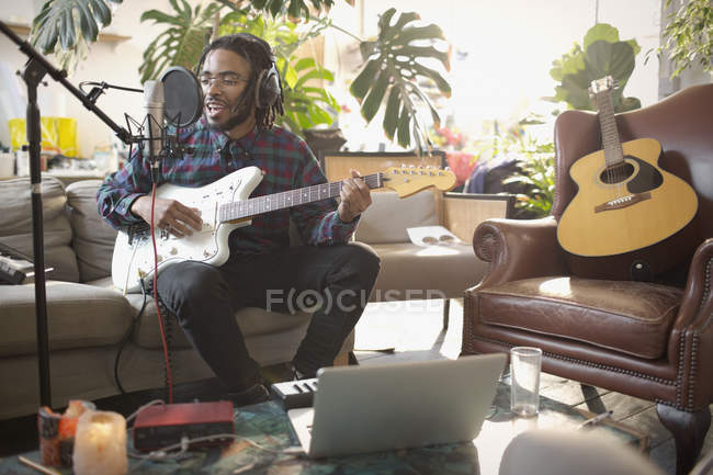 Junger männlicher Musiker nimmt Musik auf, spielt Gitarre und singt in Wohnung ins Mikrofon — Stockfoto